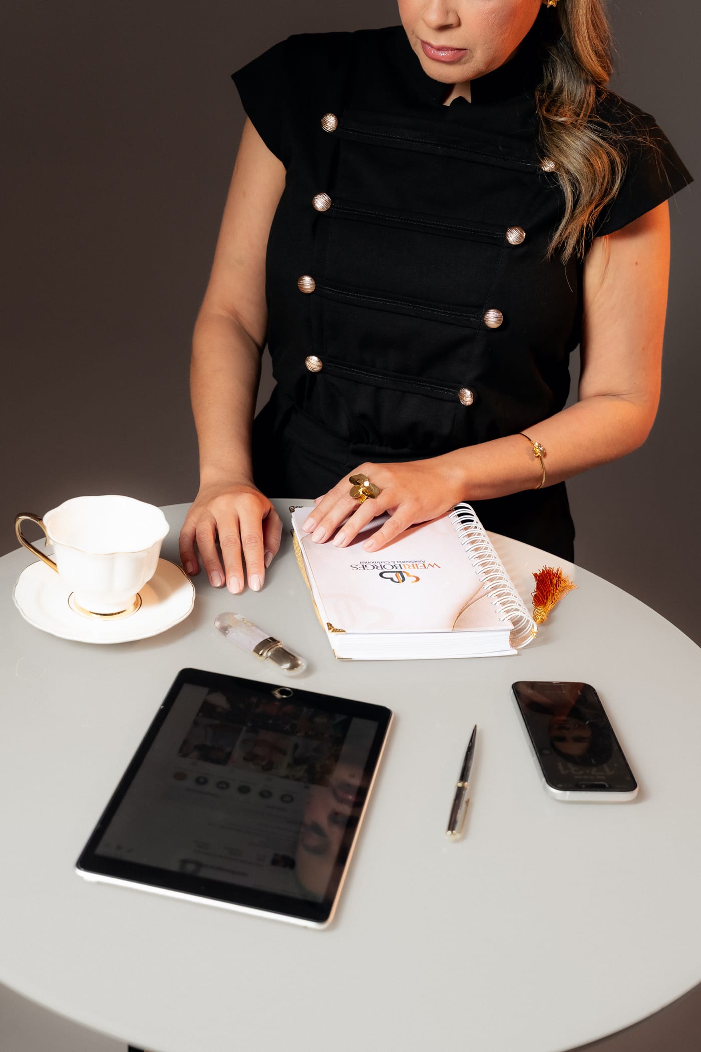 Weiri Borges à mesa com caderno de planejamento, xícara, tablet e celular.